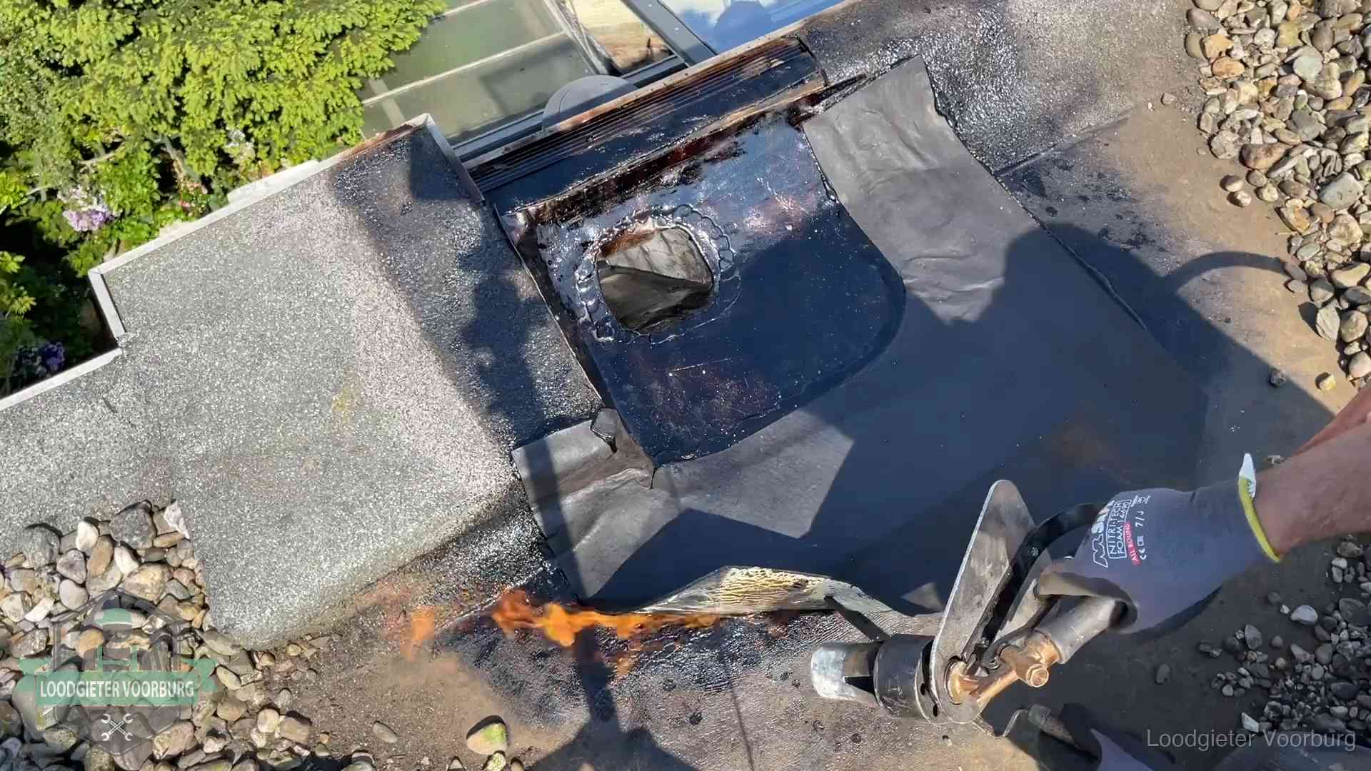 Daklekkage repareren in Voorburg Dakdekker brandt bitumen rond een doorvoer tijdens een daklekkage-reparatie in Voorburg