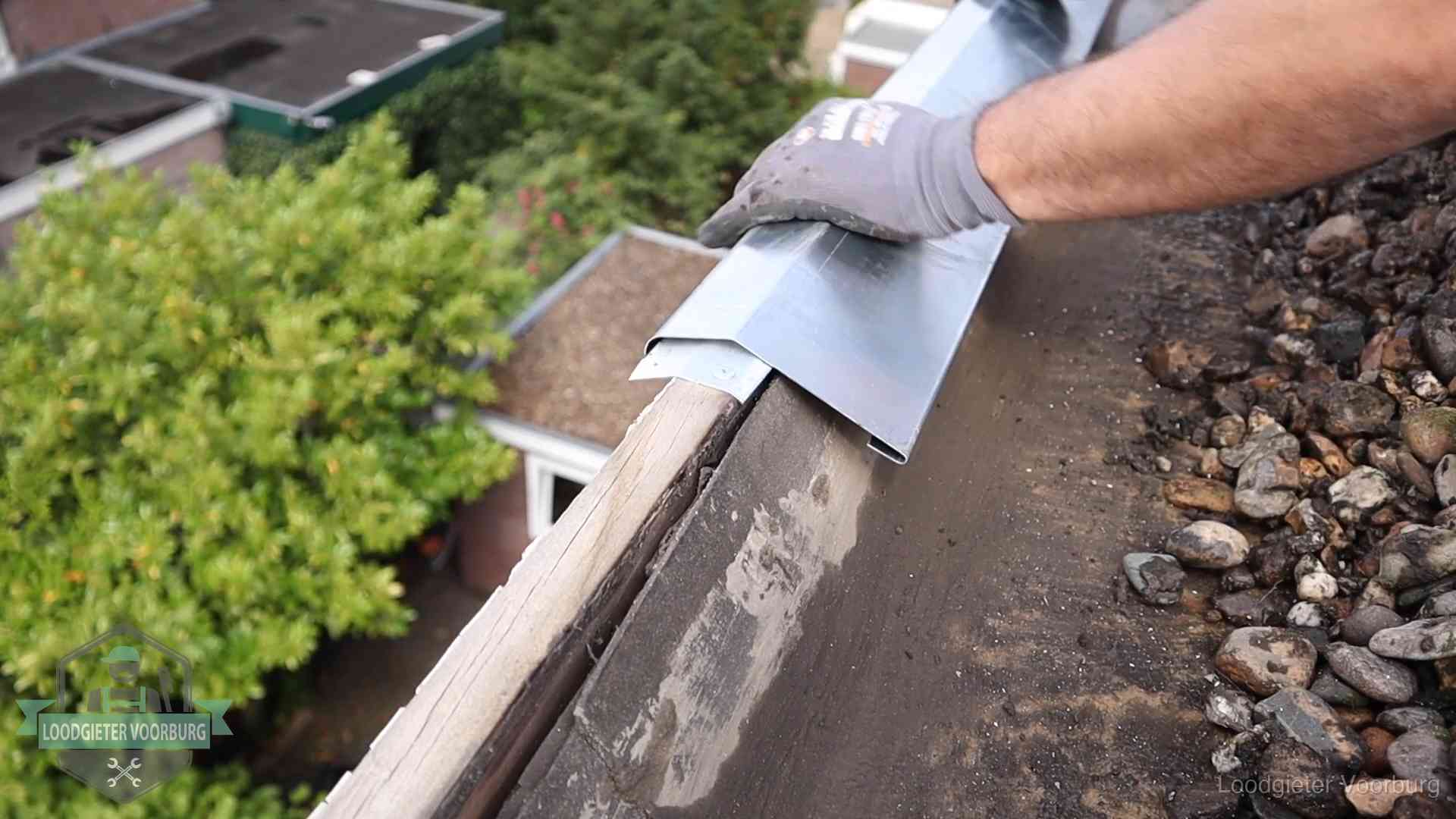 Daklekkage per wijk in Voorburg Dakdekker plaatst een zinken deklijst op een dakrand met uitzicht over een woonwijk in Voorburg