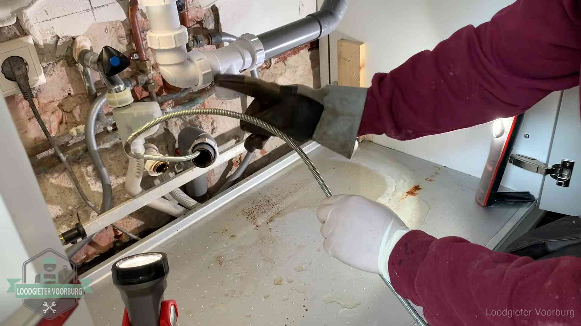 Ontstoppingsveer gaat in een geopende sifonaansluiting onder het aanrecht in Voorburg