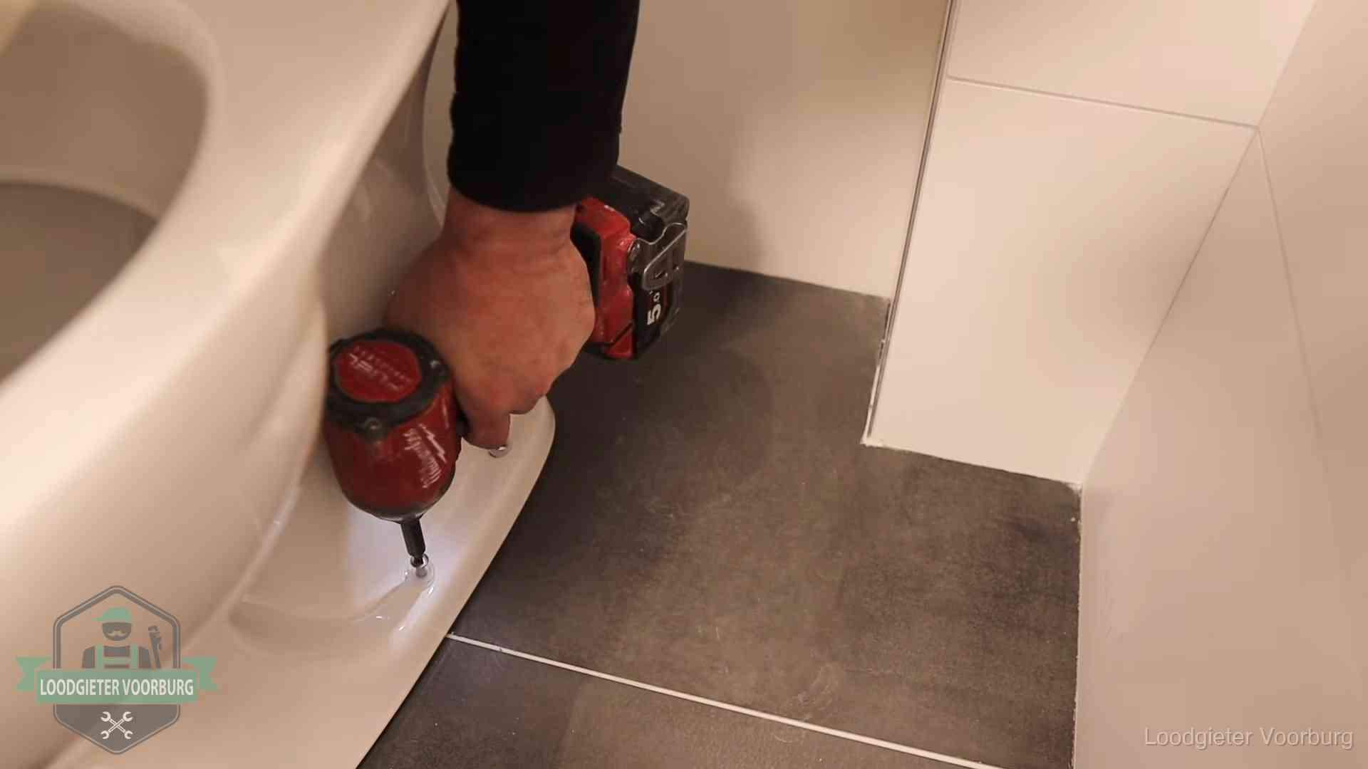 Loodgieter zet de voet van een wc-pot vast op de tegelvloer in Voorburg